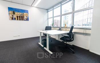 Furnished office space at Weena 290, Rotterdam Central Station featuring a desk, chairs, and large windows for natural light. Ideal for businesses seeking office space rental in a central location.