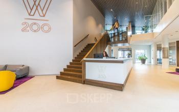 Modern office entrance at Weena 290 in Rotterdam Central Station, featuring a sleek reception desk and staircase with people engaging in business activities.