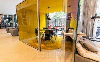 Modern furnished office space at Weena 290 with glass walls and vibrant yellow decor, ideal for collaborative meetings. Located near Rotterdam Central Station, this office to rent offers a dynamic environment.