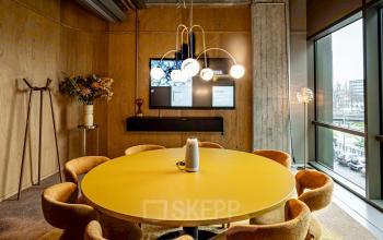 Modern office space for rent at Hofplein 19 in Rotterdam Central Station, featuring a stylish conference room with a bright yellow round table, contemporary lighting, and large windows providing natural light.