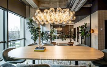 Stylish conference room at Hofplein 19 in Rotterdam Central Station with a modern chandelier, large windows, greenery, and an inviting table, ideal for office space rental.