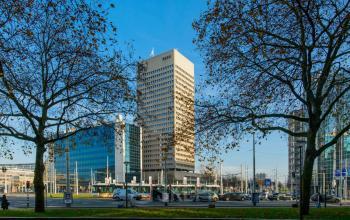 Exterior view of office building at Hofplein 20 in Rotterdam Central Station surrounded by autumn trees and busy street.