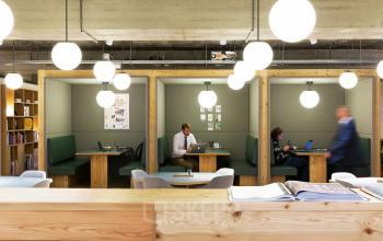Modern office space at Hofplein 20, Rotterdam Central Station, featuring cozy workspaces with wooden booths, comfortable seating, bright lighting, and professionals working on laptops.