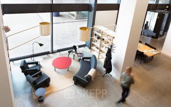 Modern office lounge area with sleek furniture and large windows, located at Hofplein 20, Rotterdam Central Station.