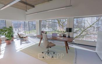 Bright office space with large windows, natural light, and a desk dominated by professional items located at Hofplein 20, Rotterdam Central Station.