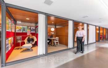 Interior view of office space at Hofplein 20, Rotterdam Central Station, with furnished meeting areas and a person talking and another seated. Ideal for office space rental.