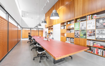 Spacious office space rental at Hofplein 20, Rotterdam Central Station, featuring a long table and shelves with books, ideal for collaborative work. Modern lighting and seating enhance the functionality.
