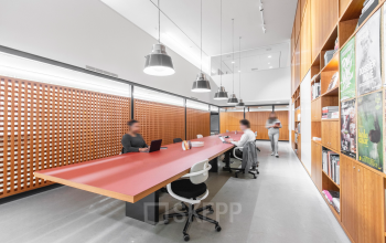 Modern office space at Hofplein 20, Rotterdam Central Station with a long shared desk, bookshelves, and people working on laptops. Ideal for office space rental.