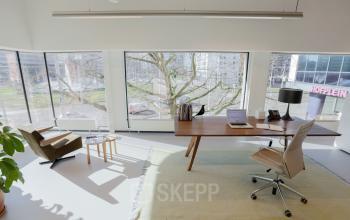 Bright office space in Hofplein 20, Rotterdam Central Station, featuring a large desk, chair, and lamp with a view of the city through large windows.