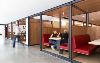Modern office to rent at Hofplein 20, Rotterdam Central Station with red booth seating and collaborative workspace design.