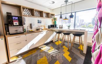 Bright and modern pantry at Weena-Zuid 130, Rotterdam Central Station, featuring a coffee machine, bar stools, and ample storage. Ideal spot in office space rental.