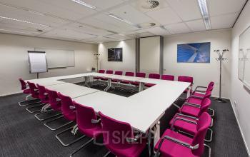 A furnished meeting room with a large U-shaped table and red chairs, perfect for office space rental at Weena-Zuid 130, Rotterdam Central Station.