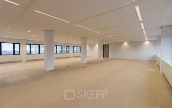 Interior view of an unfurnished office space available for rent at Weena 750 in Rotterdam Central Station, featuring large windows and ample lighting.