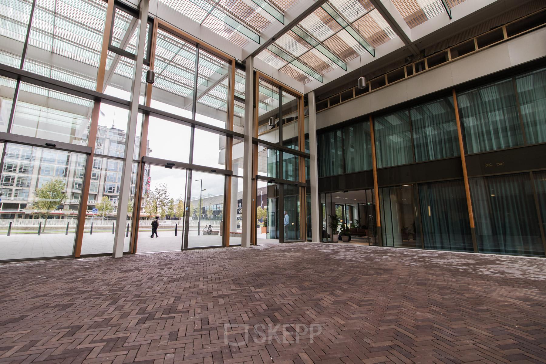 Spacious entrance area of Weena 750 office space rental at Rotterdam Central Station with large glass doors and modern architecture.