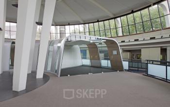 Interior view of office space rental at Kruisplein 15-25, Rotterdam Central Station, featuring modern glass-walled meeting areas under a high ceiling with natural light.