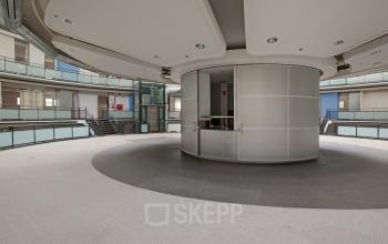 Interior view of office to rent at Kruisplein 15-25, Rotterdam Central Station, showing a modern circular space with carpeted flooring and metal accents.