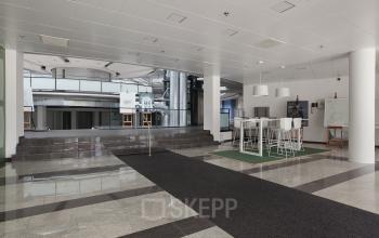 Modern interior at Kruisplein 15-25, Rotterdam Central Station with high ceilings, sleek floors, and contemporary white furniture. A space for office space rental, featuring a casual meeting area with bar-height tables.