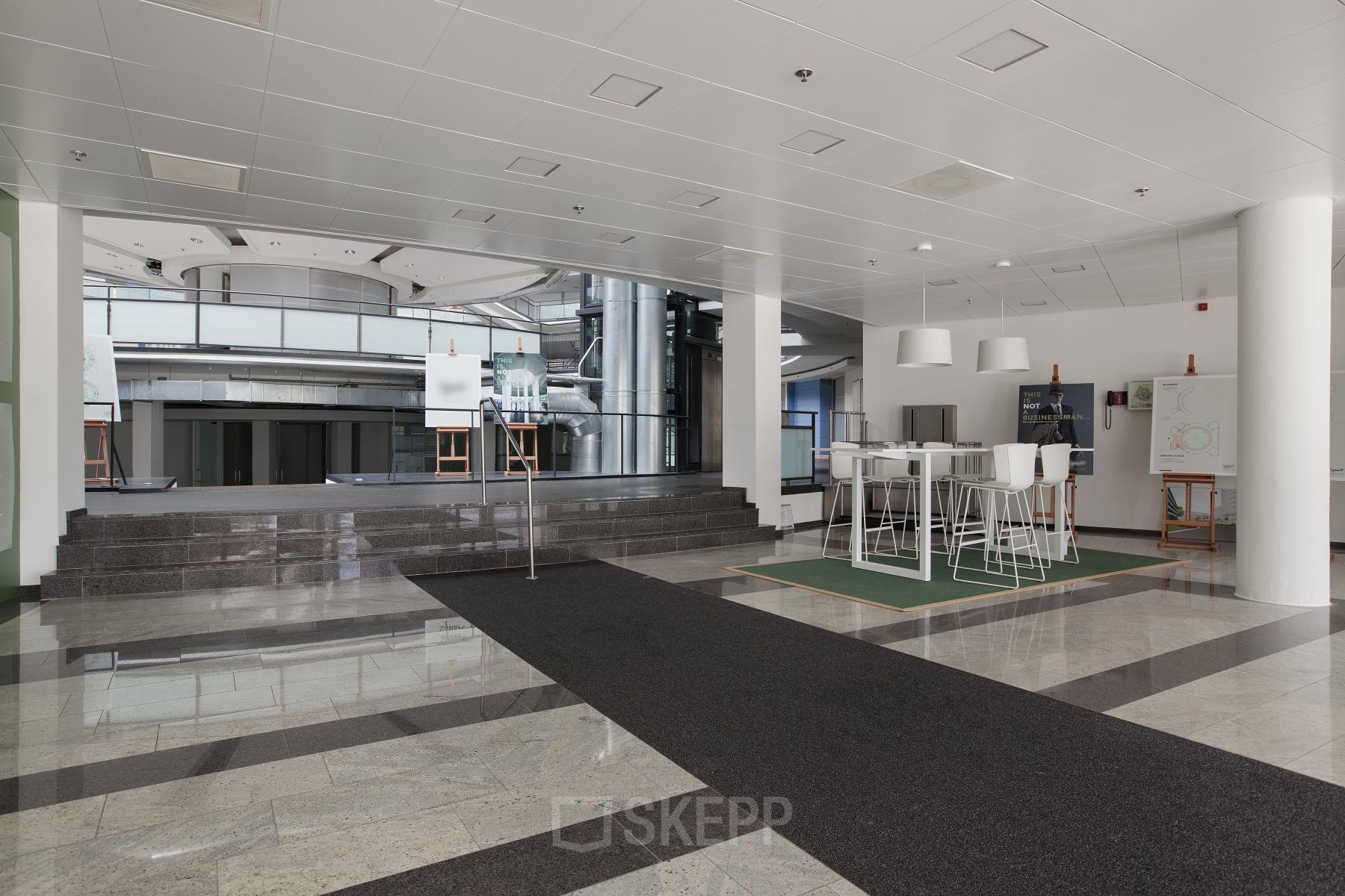 Modern interior at Kruisplein 15-25, Rotterdam Central Station with high ceilings, sleek floors, and contemporary white furniture. A space for office space rental, featuring a casual meeting area with bar-height tables.