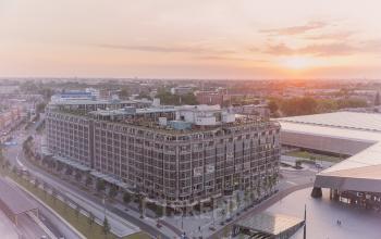 Exterior view of the office building at Stationsplein 45, Rotterdam Central Station, showcasing a modern facade with large windows and an adjacent area with green landscaping.