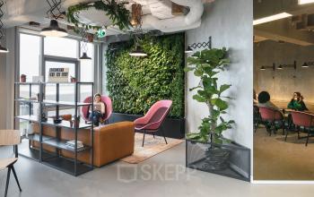 Modern office lounge area at Stationsplein 45, Rotterdam Central Station, featuring pink chairs, greenery wall, and business professionals engaged in conversation in the meeting room.