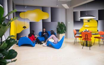 Modern office lounge at Stationsplein 45, Rotterdam Central Station with vibrant yellow and blue decor, colleagues seated in a casual meeting.