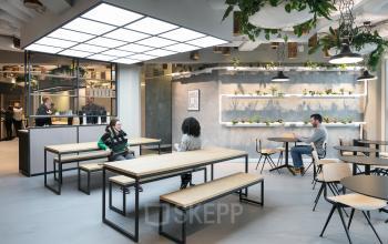 Modern office space for rent at Stationsplein 45 in Rotterdam Central Station, featuring a stylish lounge area with tables, seating, and lush greenery.
