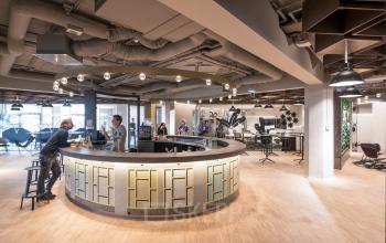 Modern office space at Stationsplein 45, Rotterdam Central Station with open floor plan, round reception desk, and business professionals engaging in discussions.