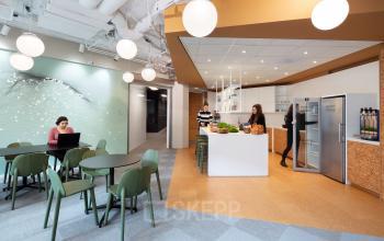 Modern office space at Stationsplein 45 in Rotterdam Centraal Station featuring a shared workspace and a kitchenette with people working and socializing.