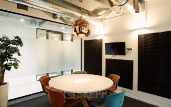 Modern office space rental at Westblaak 90, Rotterdam Center with round table, TV, colorful chairs, and industrial ceiling design.