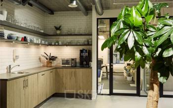 Modern pantry area in the office at Westblaak 90, Rotterdam Center, featuring wooden cabinets, a sink, coffee machine, and open shelves with glassware and dishes.