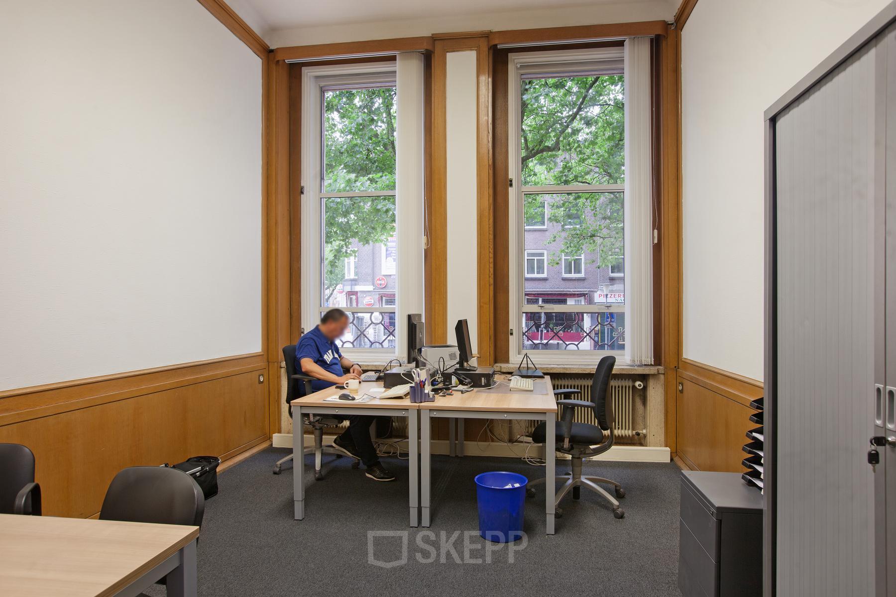 Strategic office space rental at Schiekade 830, Rotterdam Center, with a professional at work overlooking the cityscape.