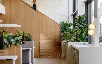 Modern office space at Vasteland 42-110, Rotterdam Center, featuring sleek workstations, wooden accents, abundant natural light, and greenery.