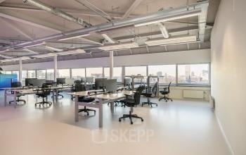 Modern office space rental at Vasteland 42-110, Rotterdam with a row of desks and computers under bright ceiling lights.
