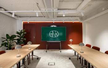 Modern conference room in office space rental at Vasteland 42-110, Rotterdam Center, featuring two long tables, chairs, lamps, and a digital screen.