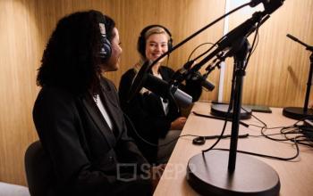 Two women in a recording studio at Vasteland 42-110, Rotterdam Center, engaging in podcast activities with microphones and headphones.