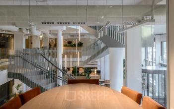 Modern office space with wooden meeting table and brown chairs, large windows, and open stairways in Rotterdam Center at Vasteland 42-110.