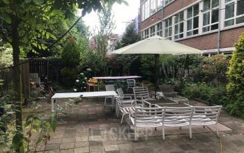 Outdoor lounge area with tables, chairs, and a large umbrella in the courtyard of an office building at Schiekade 105, Rotterdam Center.