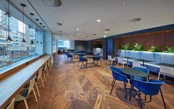 Spacious office in Blaak 555, Rotterdam Center, featuring modern workspaces with blue seating, wood flooring, and large windows ideal for office space rental.