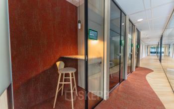 Modern office corridor at Blaak 555, Rotterdam Center, featuring stylish wooden flooring and glass-walled meeting pods. Ideal for office space rental with contemporary design and efficient layout.