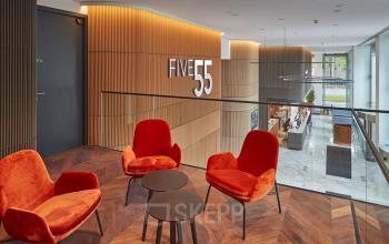 Modern office lounge area at Blaak 555, Rotterdam Center, featuring stylish red chairs and wood paneling. Ideal office space rental opportunity.