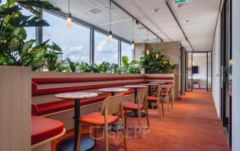 Bright workspaces at Blaak 555 in Rotterdam Center, featuring vibrant red seating and lush plants, available for office space rental.