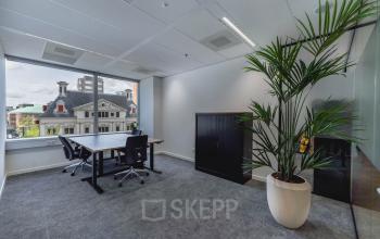 Bright office space with large window view at Blaak 555, Rotterdam Center. Ideal for office space rental with modern furnishings and a potted plant.