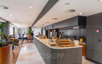 Interior of Blaak 555, Rotterdam Center, featuring a modern canteen area. A person is preparing food at the counter, suitable for office space rental.