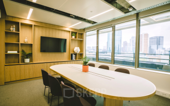 Modern furnished office space at Coolsingel 65, Rotterdam Center, featuring a large table, chairs, shelves, and a window view of the city skyline, ideal for office space rental.