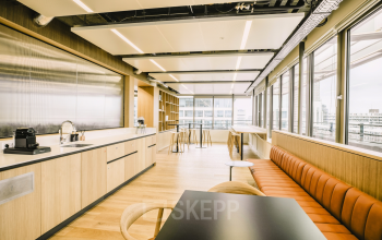Modern office space with a sleek kitchen area featuring wooden cabinetry and bar seating, located at Coolsingel 65 in Rotterdam Center, perfect for office space rental.