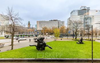 Exterior view of Weena 87 in Rotterdam Center, featuring lush green lawn and bustling street. Ideal location for office space rental.