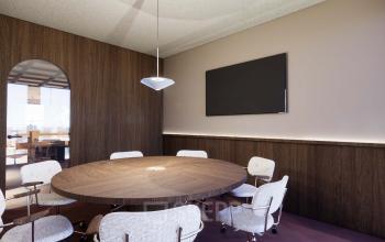 Modern conference room with a round wooden table and comfortable chairs at Coolsingel 139, Rotterdam Center, ideal for office space rental. Features a wall-mounted screen for presentations and natural lighting through a window.