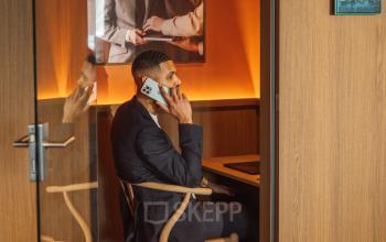 Man in a suit on a phone call in a compact, wood-accented office space at Coolsingel 139, Rotterdam Center, showcasing an office space rental option.
