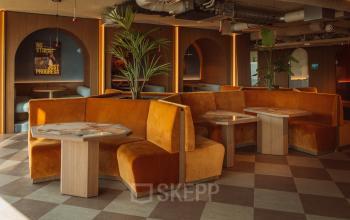 Stylish office space to rent at Coolsingel 139, Rotterdam Center, featuring orange booths and wooden tables, ideal for meetings and collaborative work.