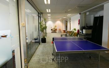 Spacious office at Wijnhaven 76, Rotterdam Center, featuring a casual meeting area with a ping pong table, plants, and seating. Ideal for office space rental.